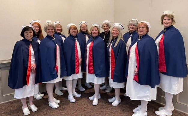 Nurses in white uniform and blue capes with red lining, as part of a nurse honor guard.